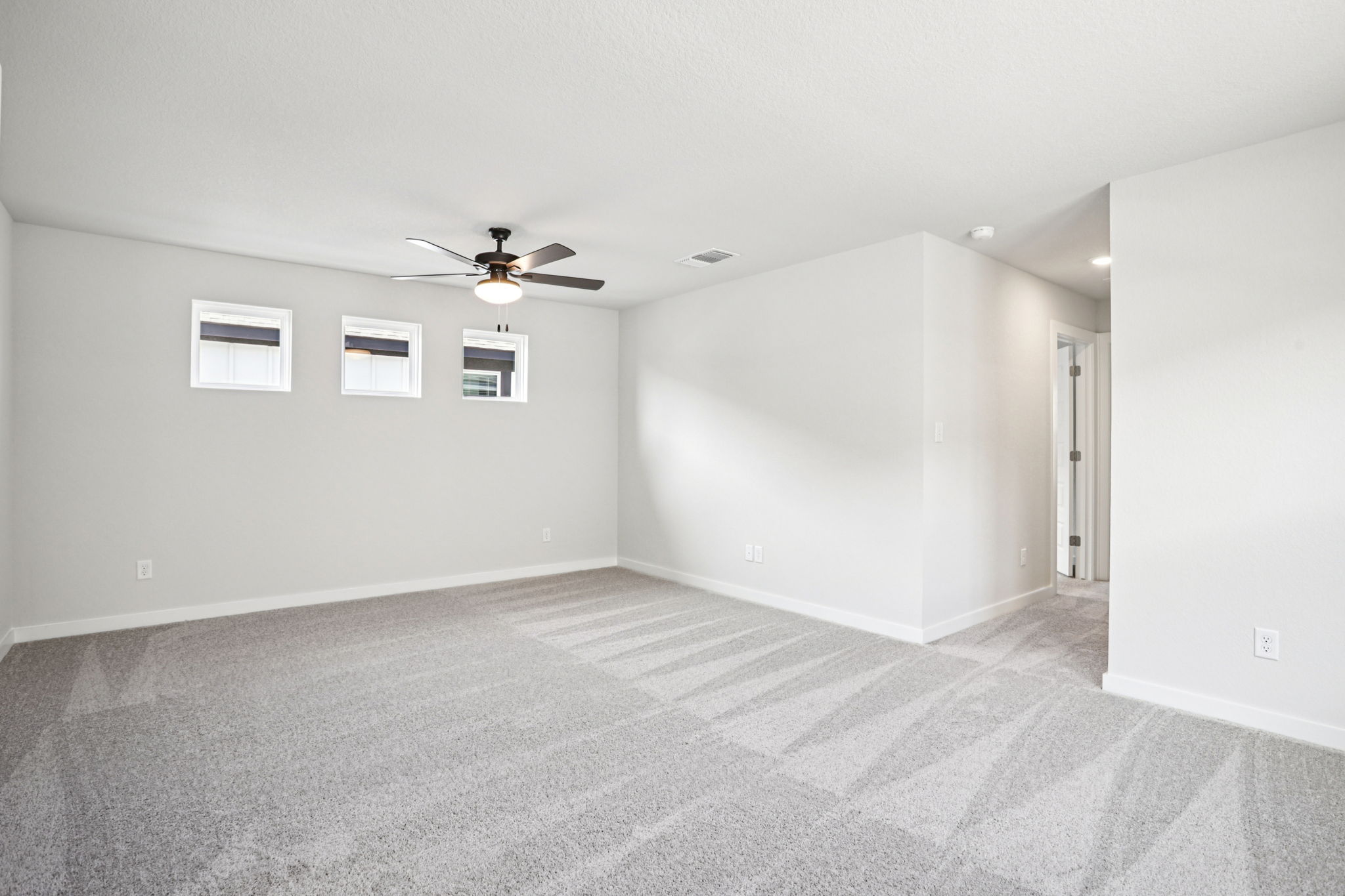 A room with a ceiling fan and a carpet.