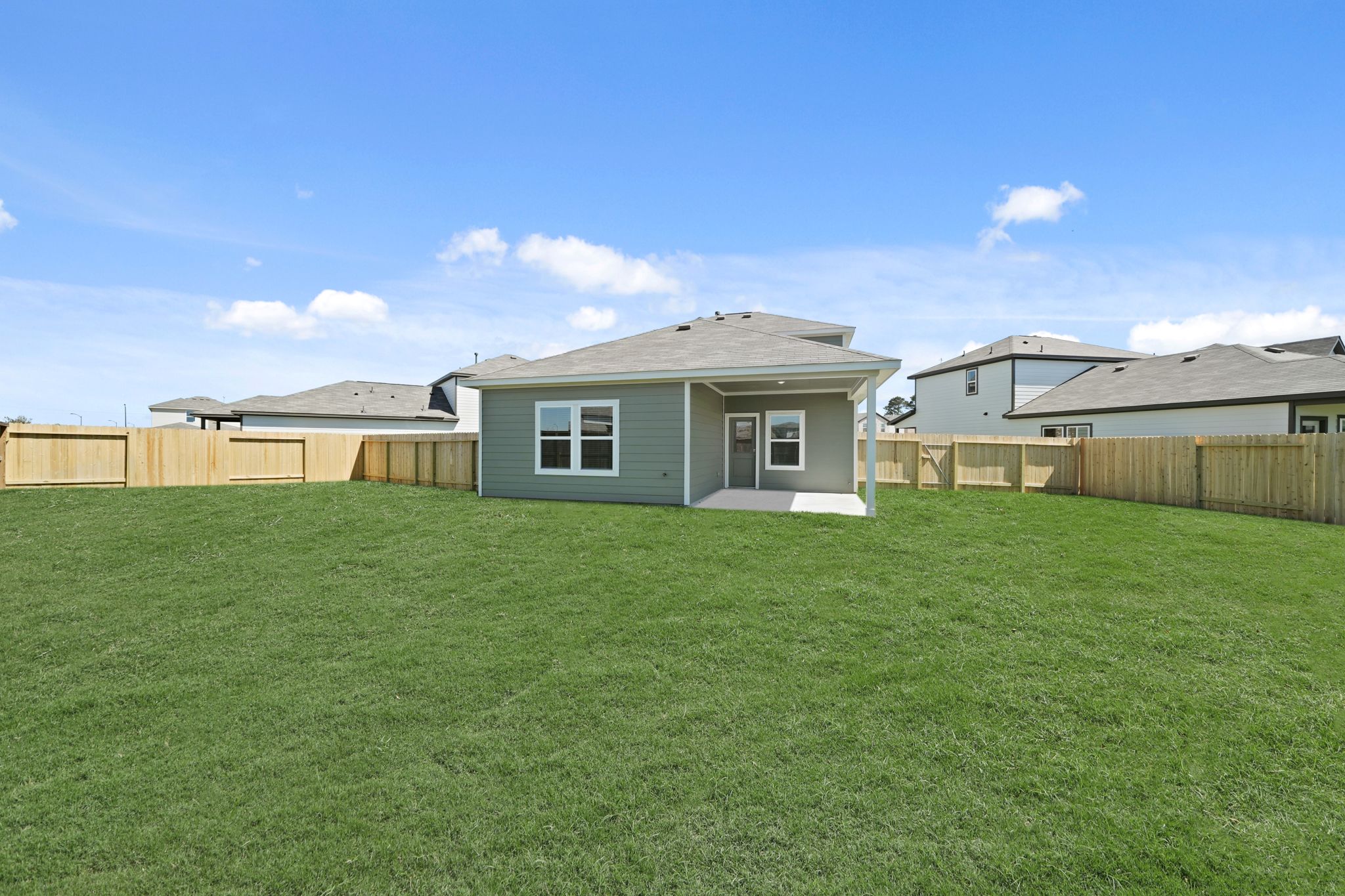 A green lawn with a fence and houses in the background.