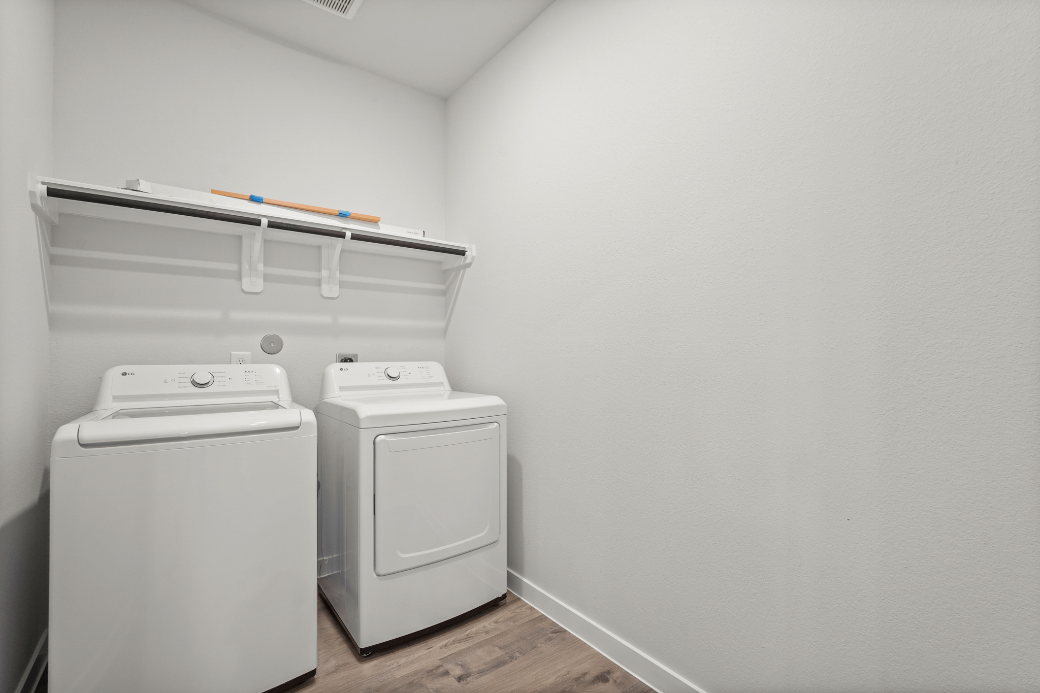 A white laundry room with a white shelf and a white laundry machine.