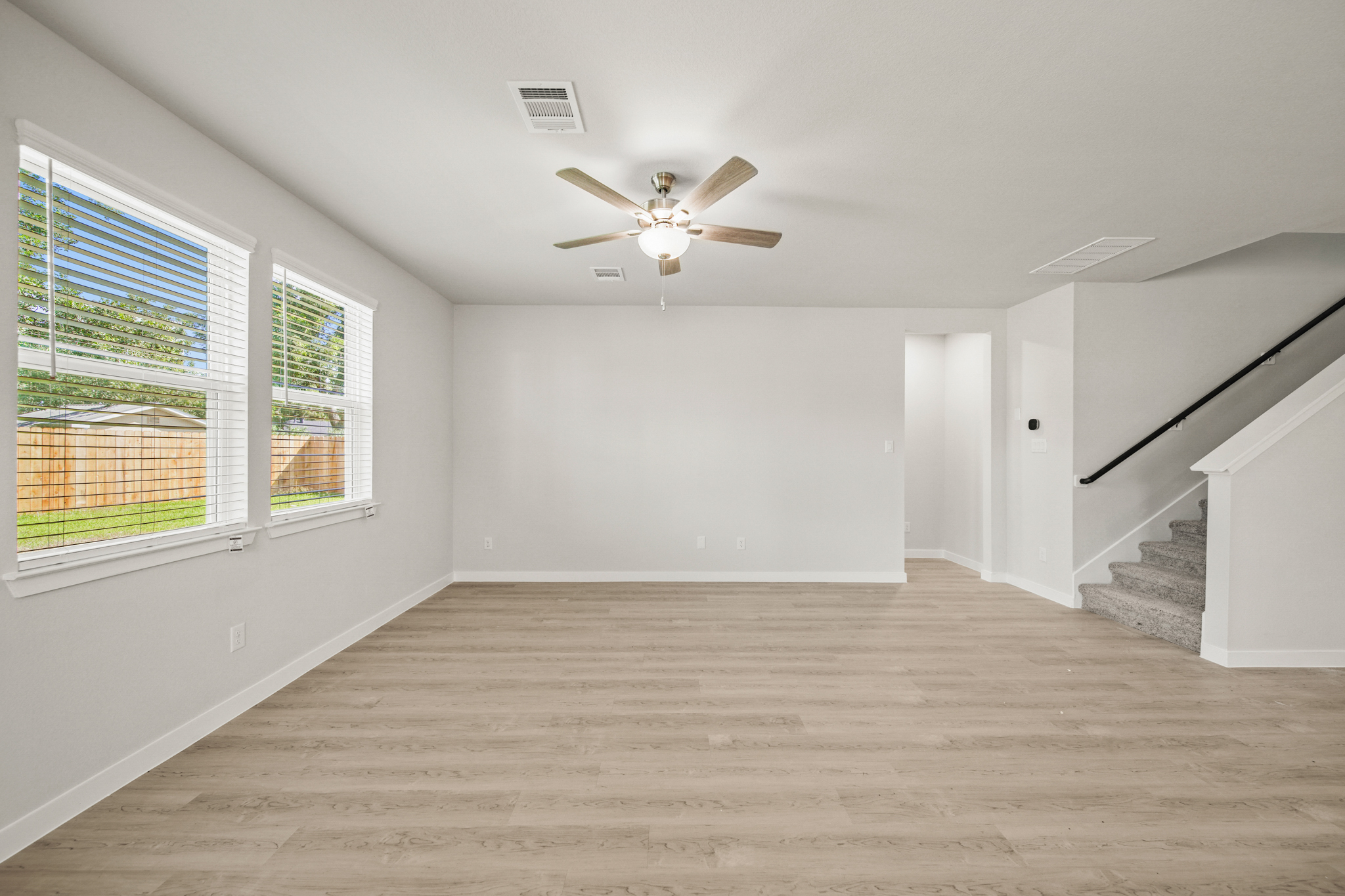 A room with a wood floor and a ceiling fan and windows.