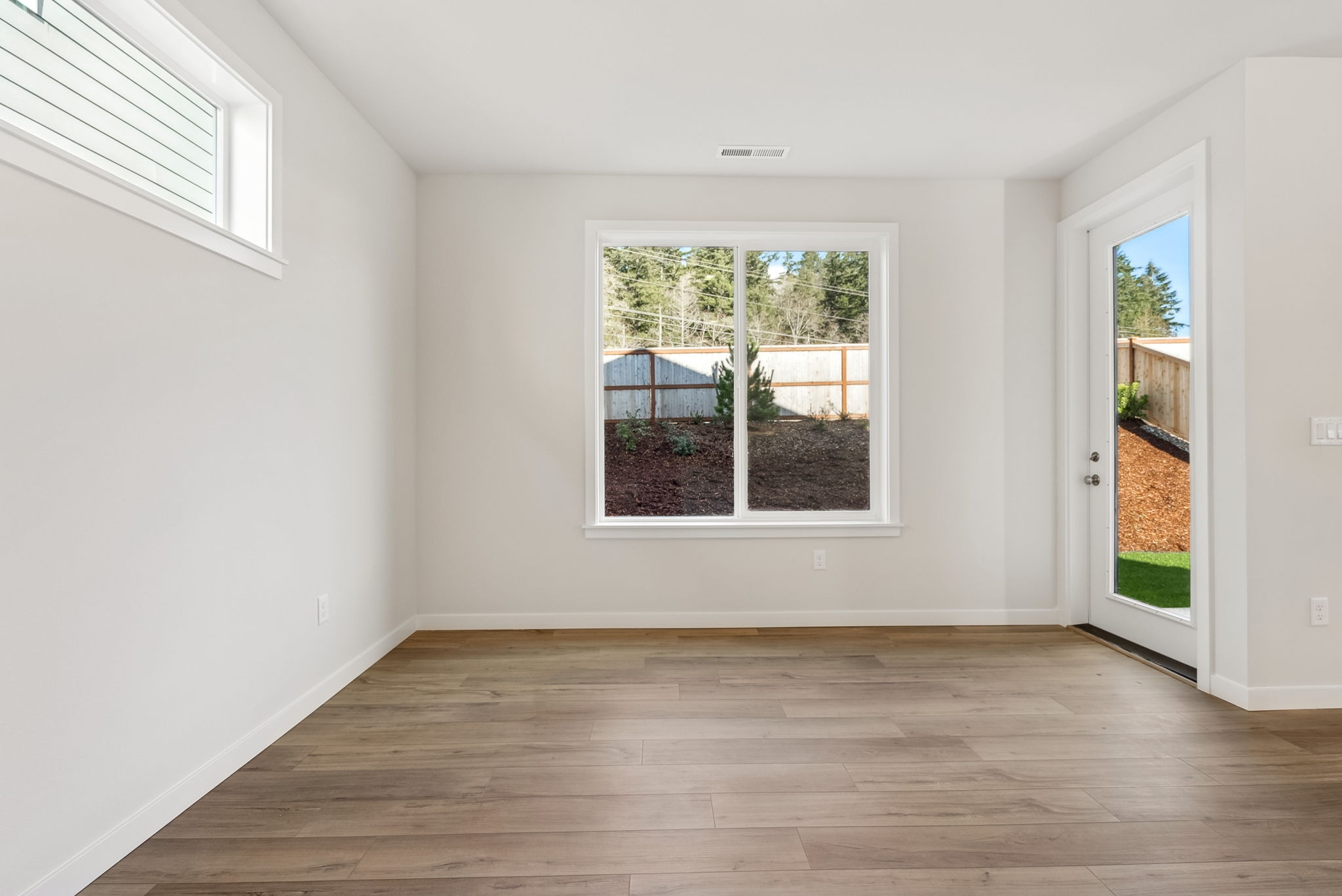 A room with a wood floor and a window with a view of the yard and a wood floor.